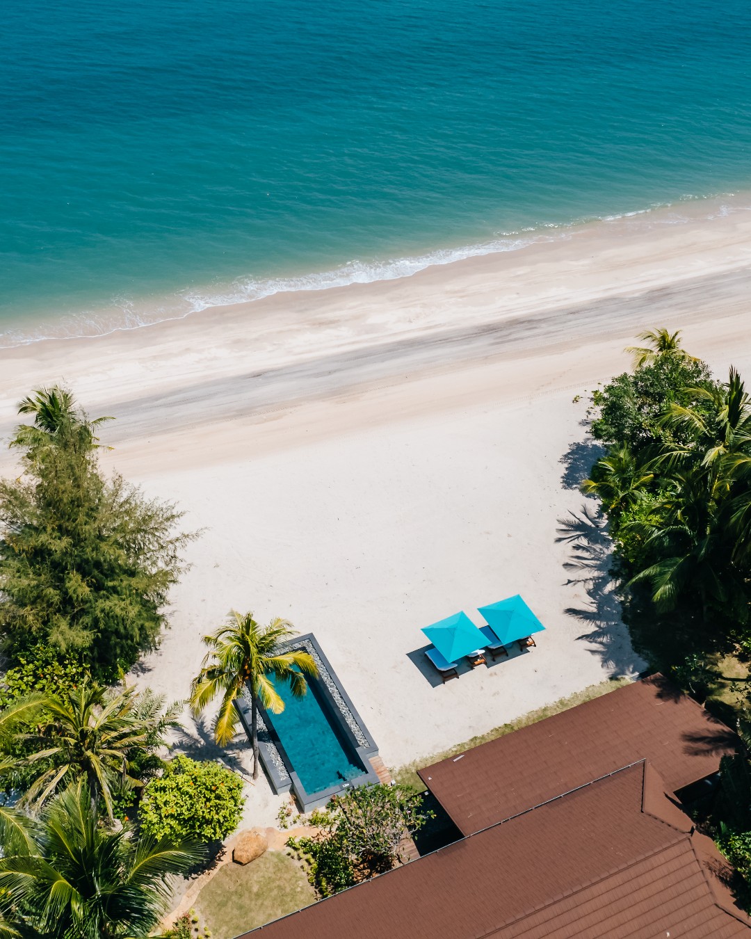 Aerial view of Four Seasons Resort Langkawi beachfront with a private pool, palm trees, sun loungers, and turquoise sea.