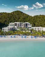 Aerial view of The St. Regis Langkawi beachfront resort with grand architecture, palm-lined beach, blue umbrellas, and lush rainforest backdrop.