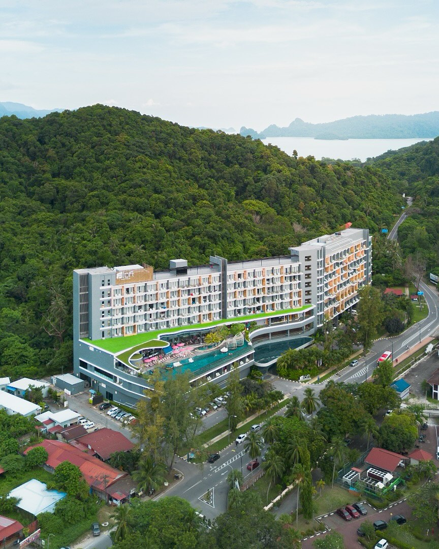 Aloft Langkawi Pantai Tengah featuring a modern hillside resort with contemporary architecture, an elevated infinity pool, lush rainforest surroundings, and scenic views toward the Andaman Sea near Pantai Tengah.