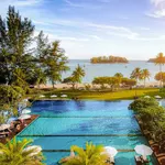 View from a balcony at The Danna Langkawi overlooking an infinity pool, palm trees, beach, and a small island in the sea.