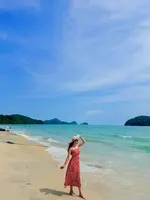 Woman in a red dress walking along the beach near Frangipani Langkawi Resort with turquoise water and island views.