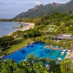 Aerial view of The Danna Langkawi with a large pool surrounded by lush greenery and a sandy beach with mountains in the background.