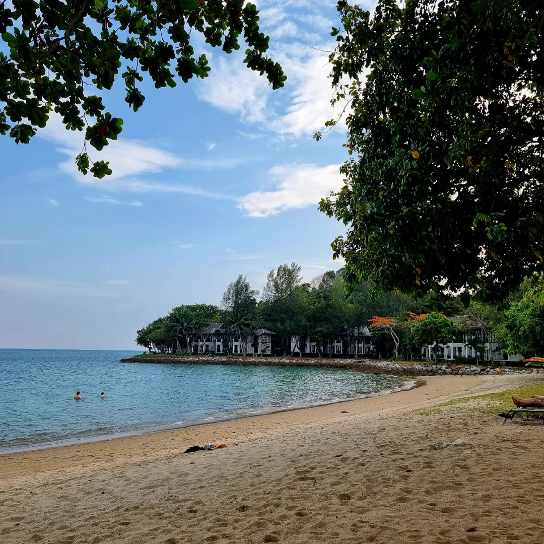 Quiet beach at Rebak Island Resort Langkawi with calm sea, shaded trees, and beachfront villas along the shoreline.