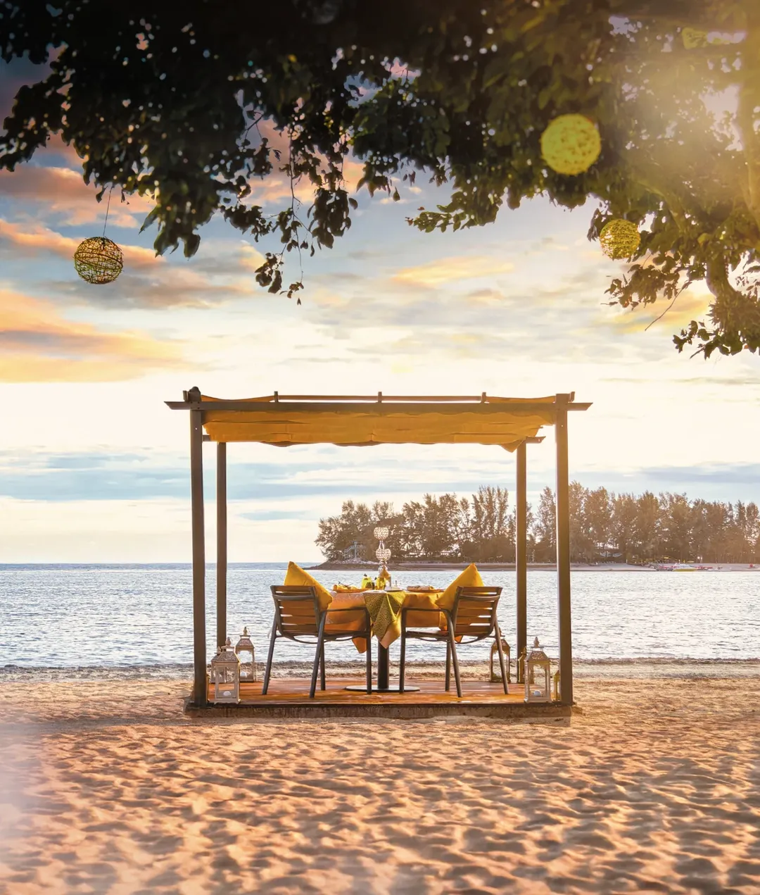 Private beachfront dining setup at The Danna Langkawi with a table under a canopy, overlooking the sea at sunset.
