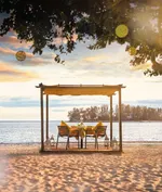 Private beachfront dining setup at The Danna Langkawi with a table under a canopy, overlooking the sea at sunset.