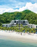 St. Regis Langkawi beachfront resort with palm trees, white sandy beach, and lush green hills in the background.