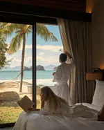 Couple relaxing in a room at Four Seasons Resort Langkawi with a beach and sea view through large windows.