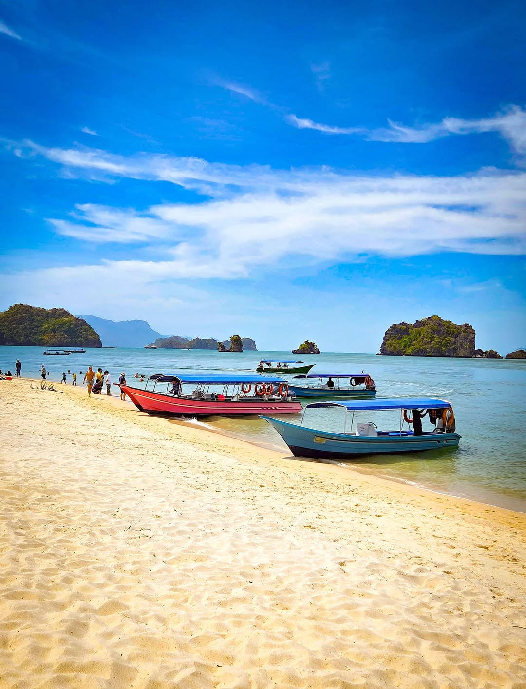 Boats lined up along the sandy shore at Tanjung Rhu Langkawi with clear blue skies and nearby islands.