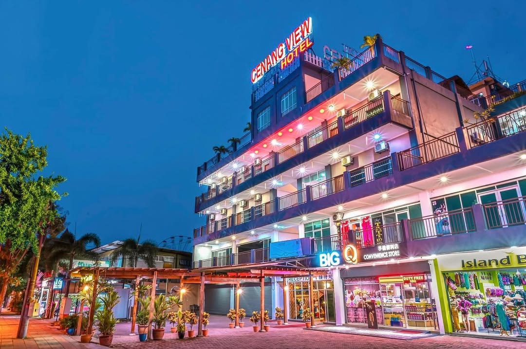 Cenang View Hotel Langkawi featuring a vibrant multi-story hotel illuminated at night, with rooftop signage, street-level shops, colorful lighting, and a lively location near Pantai Cenang.