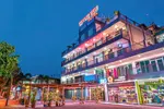 Cenang View Hotel Langkawi featuring a vibrant multi-story hotel illuminated at night, with rooftop signage, street-level shops, colorful lighting, and a lively location near Pantai Cenang.