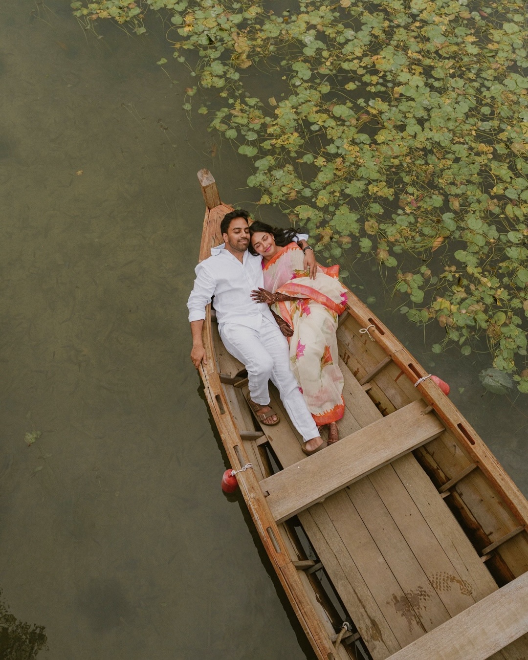 Couple relaxing in a wooden boat at The Westin Langkawi surrounded by calm water and floating greenery.
