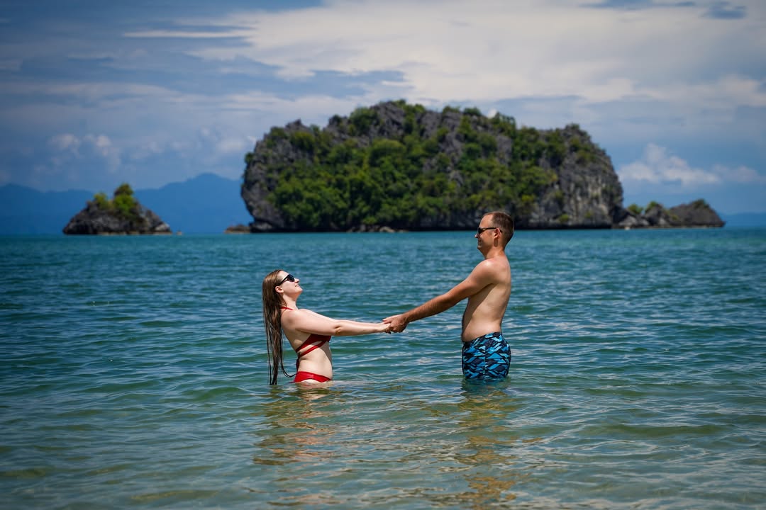 Couple standing in shallow sea at Tanjung Rhu Langkawi holding hands with a small island in the background.
