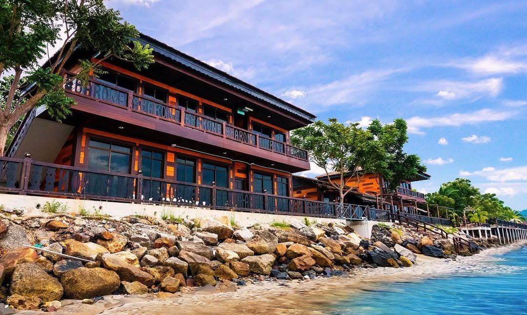 De Baron Resort Langkawi featuring a traditional Malay-inspired beachfront resort with wooden architecture, spacious sea-facing balconies, and a rocky shoreline overlooking the calm waters of Kuah Bay.