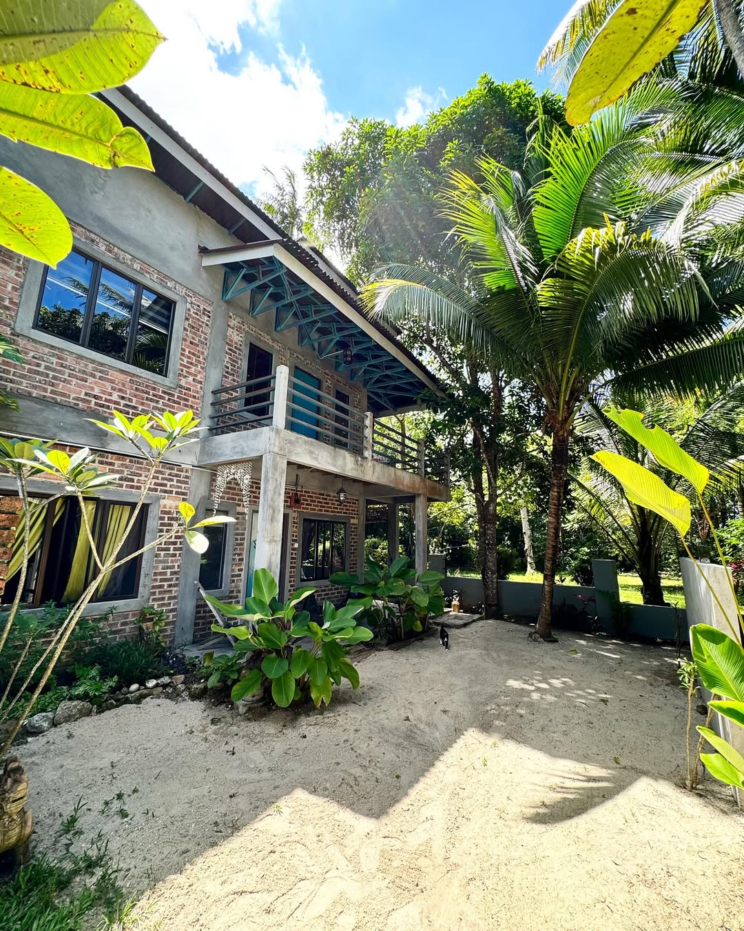 Eagleye Langkawi featuring a rustic tropical guesthouse with exposed brick and concrete architecture, spacious balconies, lush palm trees, and a peaceful garden setting surrounded by tropical greenery.