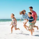 Family running and playing on the beach at Tanjung Rhu Langkawi with the sea and blue sky in the background.