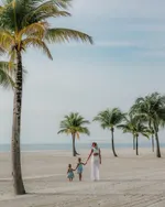 A family walking along a sandy beach at Four Seasons Resort Langkawi with palm trees and calm sea in the background.