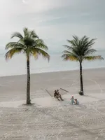 Family relaxing on a hammock between palm trees at Four Seasons Langkawi with children playing on the sandy beach by the sea.