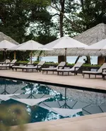 Family pool at The Datai Langkawi with sun loungers, umbrellas, and thatched cabanas overlooking the sea.