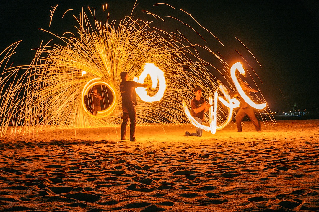 Fire performance on the beach at Berjaya Langkawi Resort with performers creating glowing trails of sparks at night.