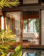 Four Seasons Resort Langkawi featuring a luxurious beachfront villa with warm timber architecture, floor-to-ceiling glass doors, elegant bedroom interiors, lush tropical landscaping, and serene ocean views.