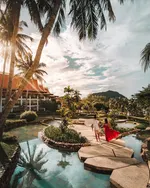 Couple walking across a garden path at The Westin Langkawi surrounded by tropical greenery, water features, and resort buildings.