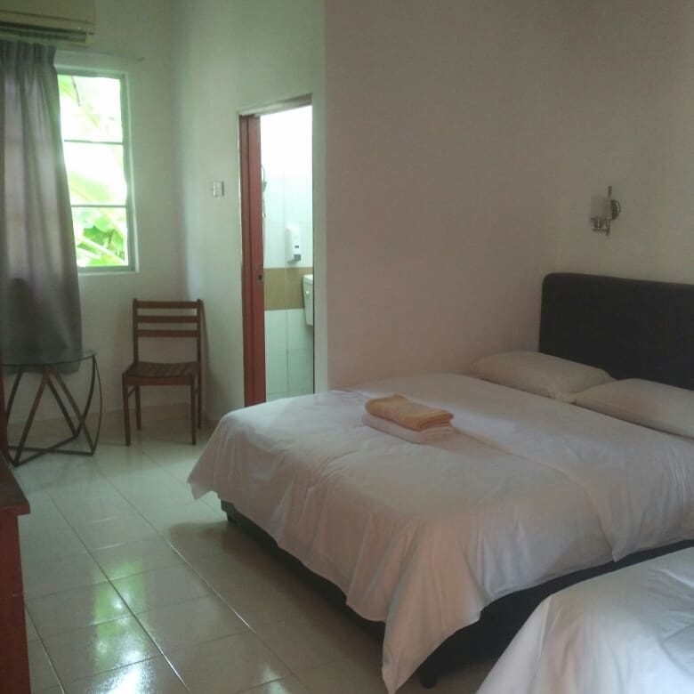 Simple guest room at Sweet Inn Langkawi with twin beds, tiled floor, and a window letting in natural light.