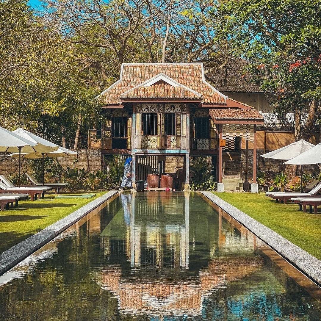 Traditional heritage villa overlooking a long reflective pool at Temple Tree at Bon Ton, surrounded by lush gardens and sun loungers in Langkawi.