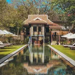 Traditional heritage villa overlooking a long reflective pool at Temple Tree at Bon Ton, surrounded by lush gardens and sun loungers in Langkawi.