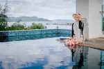 Woman sitting by an infinity pool at Adya Hotel Langkawi overlooking the sea and distant hills.