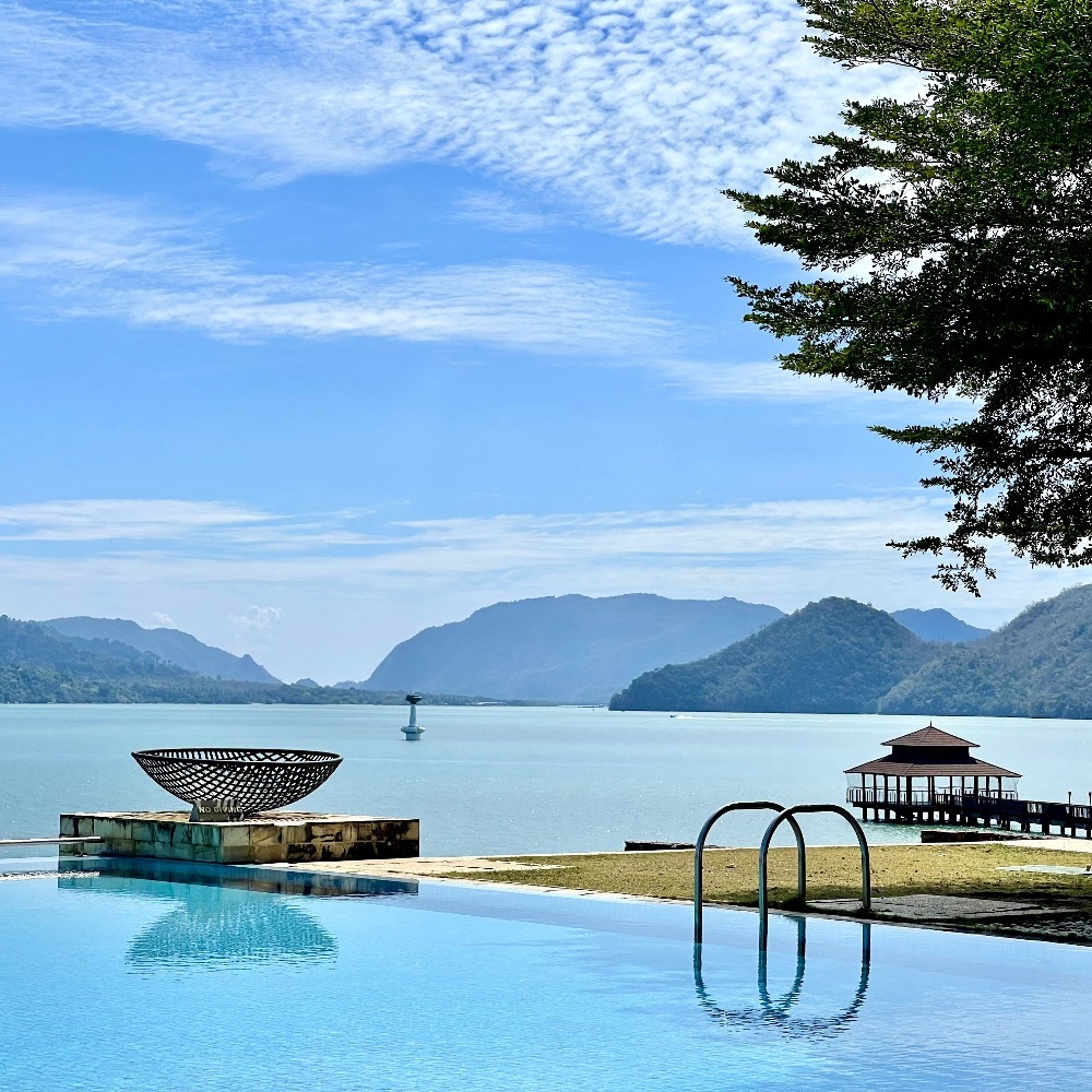 Infinity pool at The Westin Langkawi overlooking calm sea with distant mountains and a jetty pavilion.
