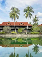 Traditional wooden building at Meritus Pelangi Beach Resort & Spa Langkawi reflected in a calm lagoon with palm trees.