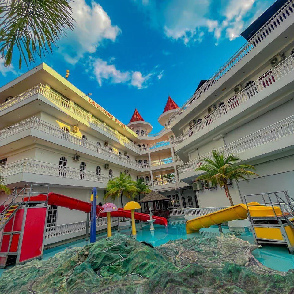Landcons Hotel Langkawi featuring a family-friendly courtyard with a swimming pool, colorful children's water slides, tropical palm trees, and distinctive castle-inspired architecture with red turret rooftops.
