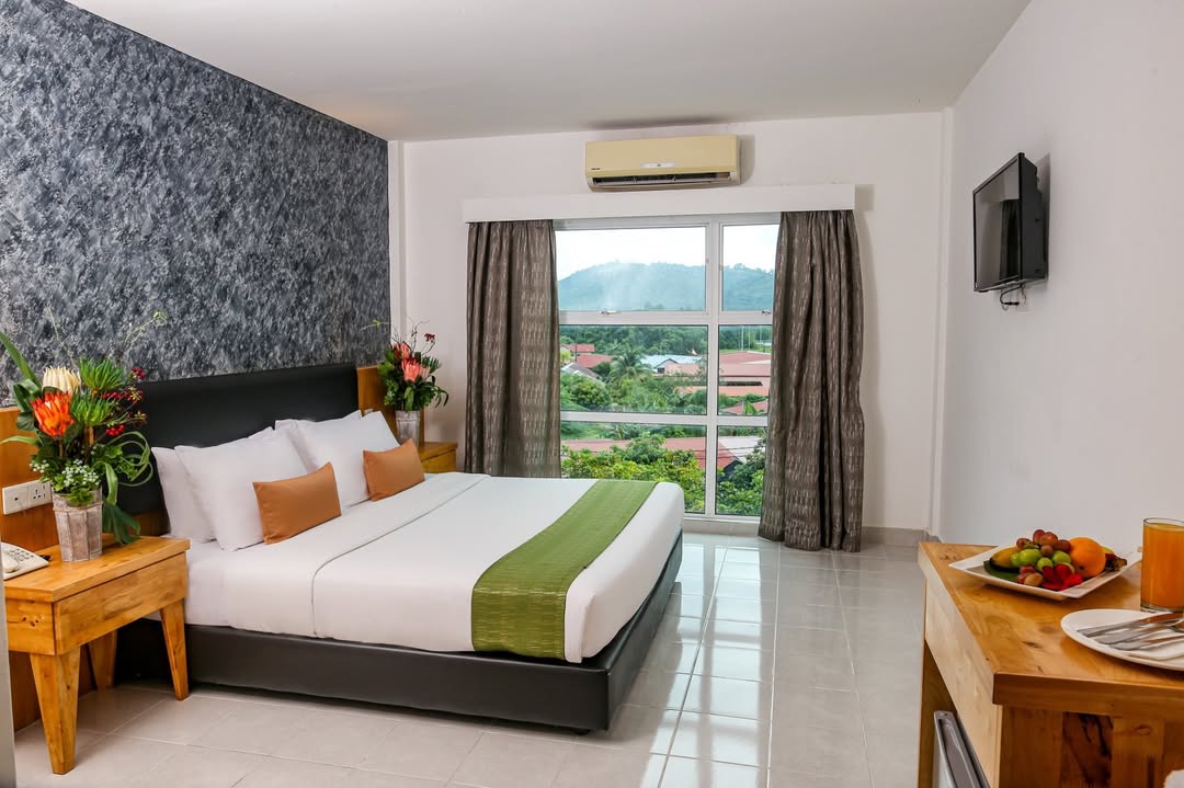 Langkapuri Resort Langkawi featuring a bright and spacious guest room with a king-size bed, wooden furnishings, large windows overlooking lush hills, and modern amenities in a comfortable tropical setting.