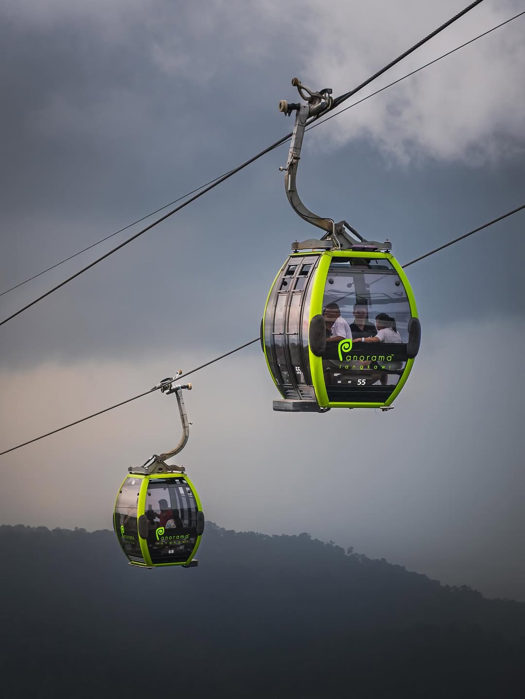 Langkawi Cable Car gondolas suspended over forested hills with cloudy skies in the background.