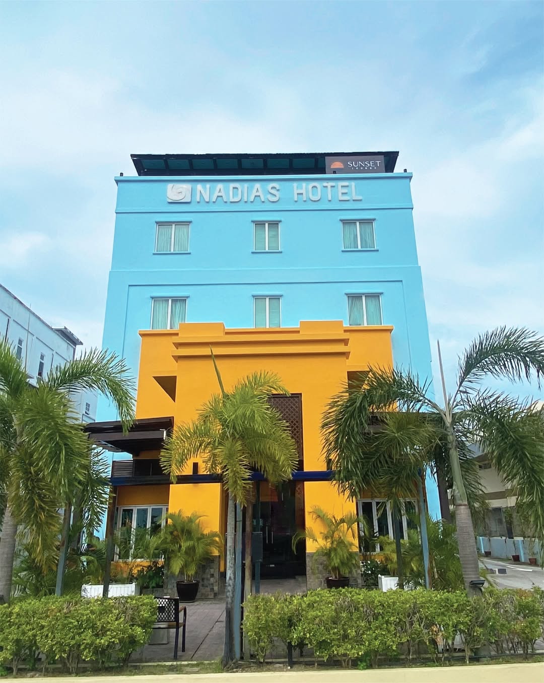 Nadias Hotel Cenang Langkawi featuring a colorful modern hotel façade with vibrant blue and yellow architecture, tropical palm trees, and a convenient location near Pantai Cenang.