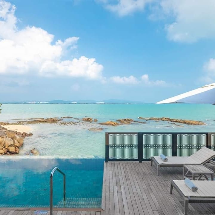 Oceanfront infinity pool at The Ritz-Carlton Langkawi with sun loungers, wooden deck, and views of rocky shoreline and turquoise sea.
