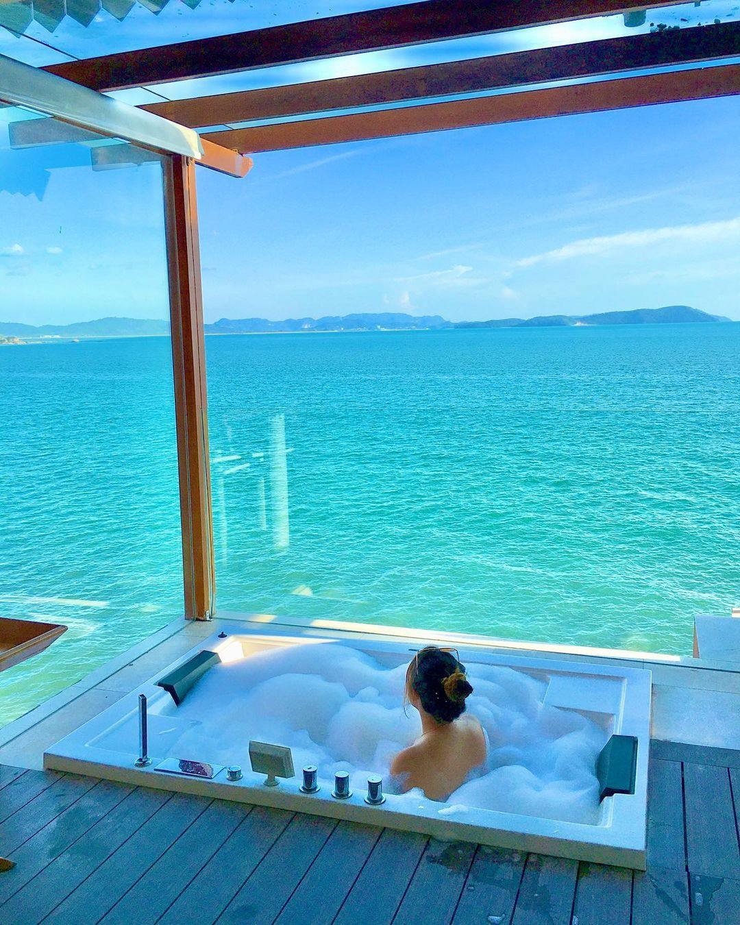 Person relaxing in a bubble bath at Berjaya Langkawi Resort with a panoramic view of the turquoise sea and distant islands.