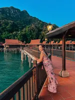 Woman standing on a boardwalk at Berjaya Langkawi Resort overlooking overwater chalets, turquoise sea, and forested hills.