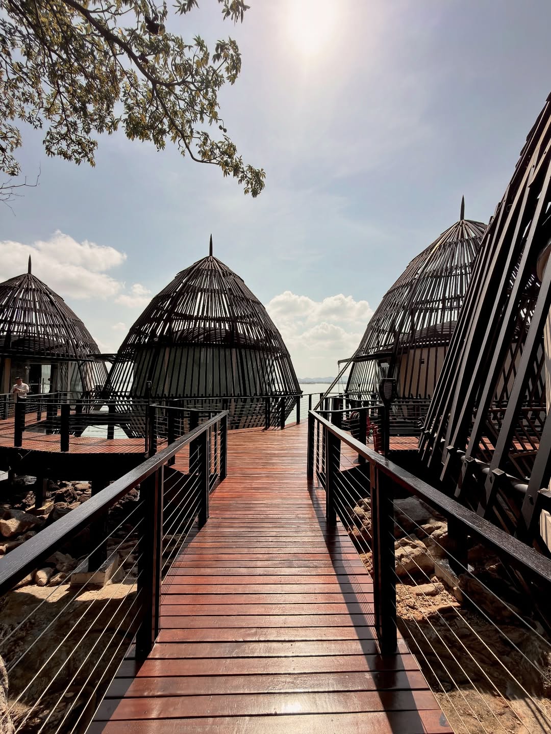 Wooden walkway leading to unique dome-shaped overwater structures with open lattice design, set against the sea in Langkawi.