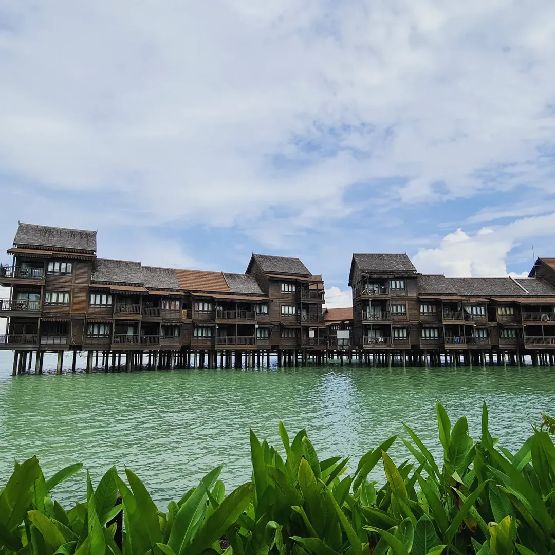 Overwater villas at Langkawi Lagoon Resort set above calm green waters with tropical plants in the foreground.