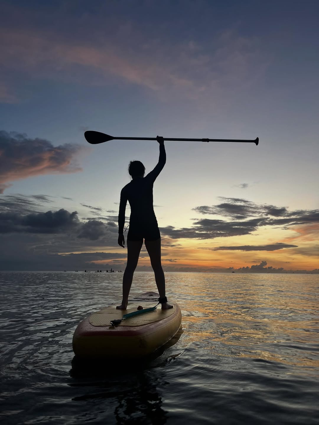 Silhouette of a person paddleboarding at sunset at Tanjung Rhu Beach Langkawi with calm sea and colorful sky.