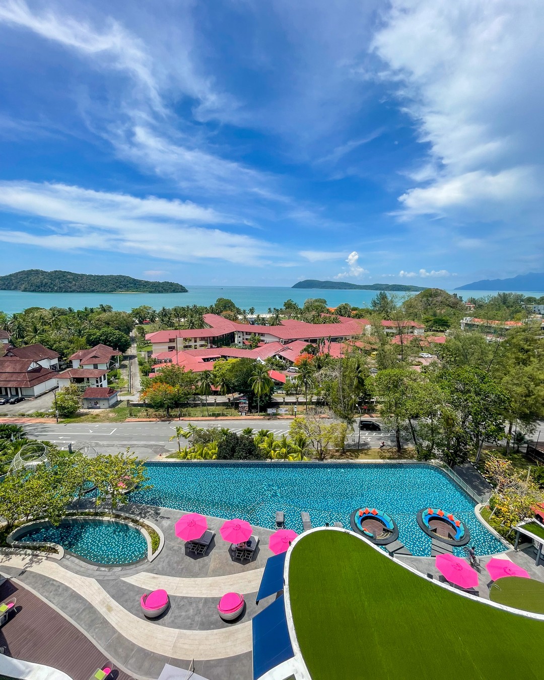 Aerial view of Aloft Langkawi Pantai Tengah with a large pool, colorful loungers, and views of the sea and nearby islands.