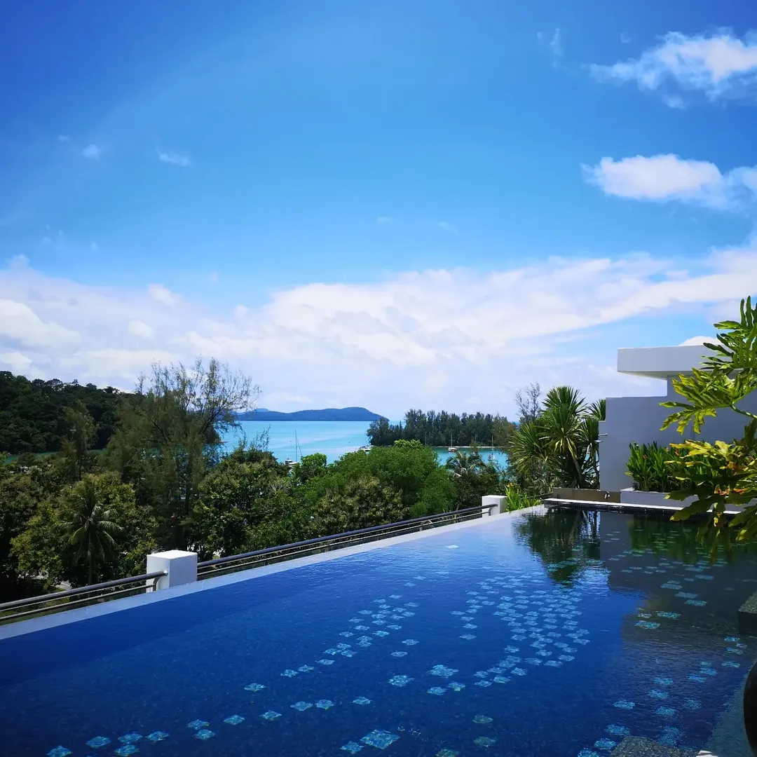Private infinity pool at The Danna Langkawi overlooking lush greenery, coastline, and turquoise sea under a blue sky.