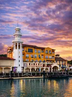 Resorts World Langkawi featuring a colorful waterfront resort with a distinctive white lighthouse, marina promenade, Mediterranean-inspired architecture, and beautiful sunset views overlooking the Andaman Sea.