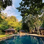 Saujana Private Villas Langkawi featuring a tranquil infinity-style swimming pool surrounded by luxury private villas, towering rainforest trees, traditional pavilions, and lush tropical landscapes in a secluded nature retreat.