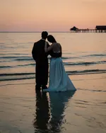 Couple standing on the beach at Berjaya Langkawi Resort during sunset with calm waves and a jetty in the background.