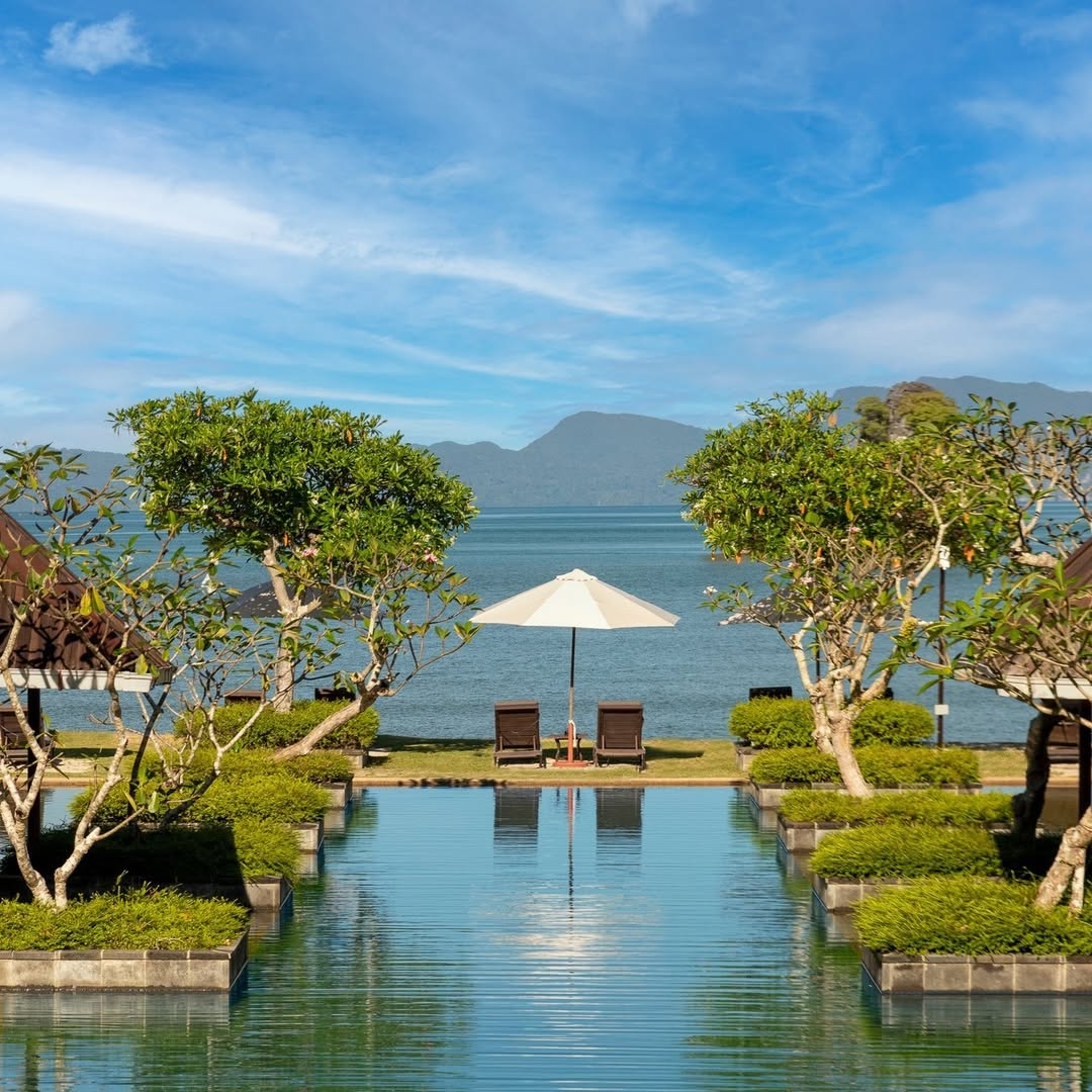 Symmetrical pool at Tanjung Rhu Resort Langkawi overlooking the calm sea, with lounge chairs, an umbrella, and distant mountains.