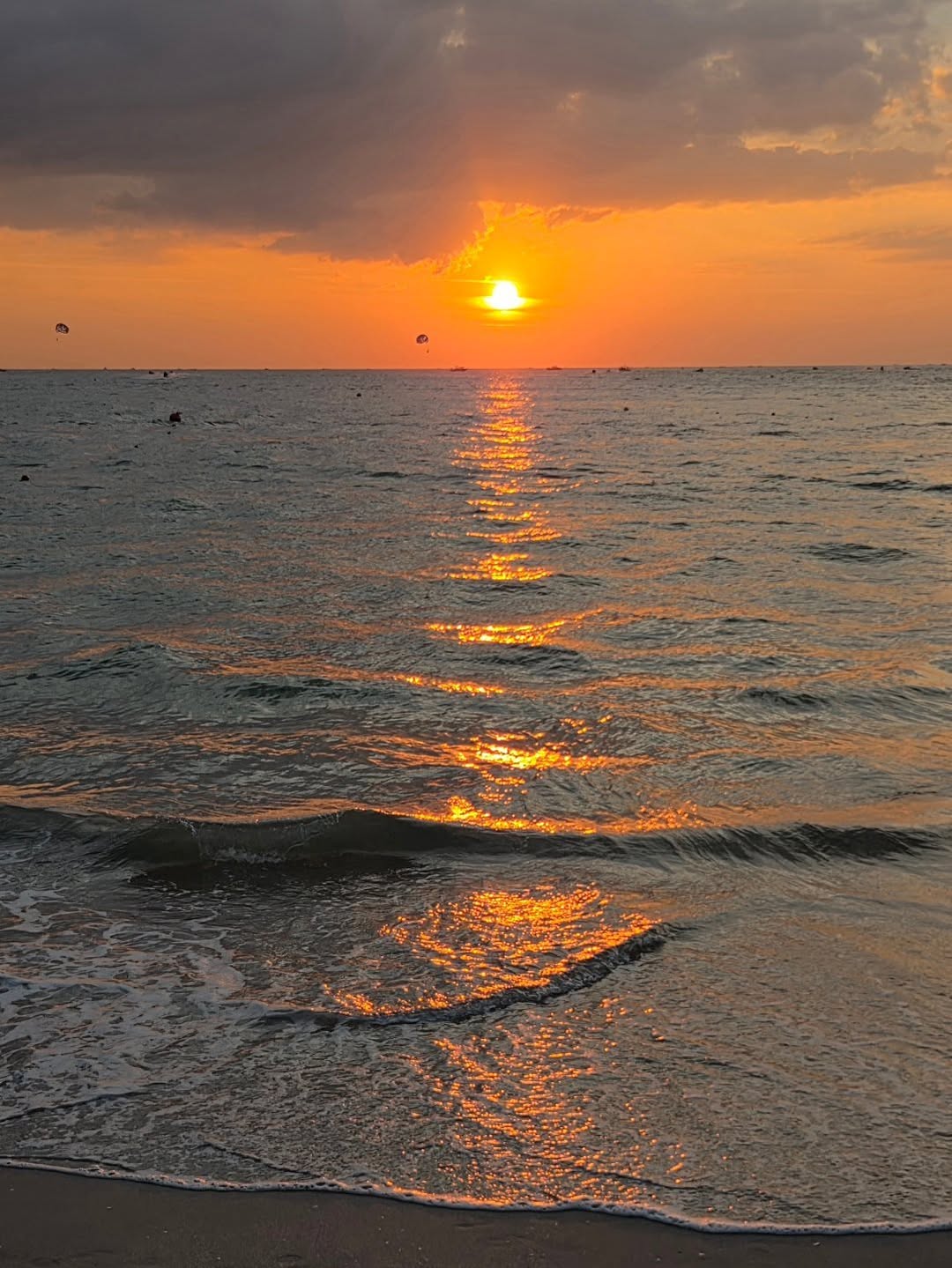 Sunset at Pantai Cenang Langkawi with golden reflections on gentle waves and a cloudy sky.