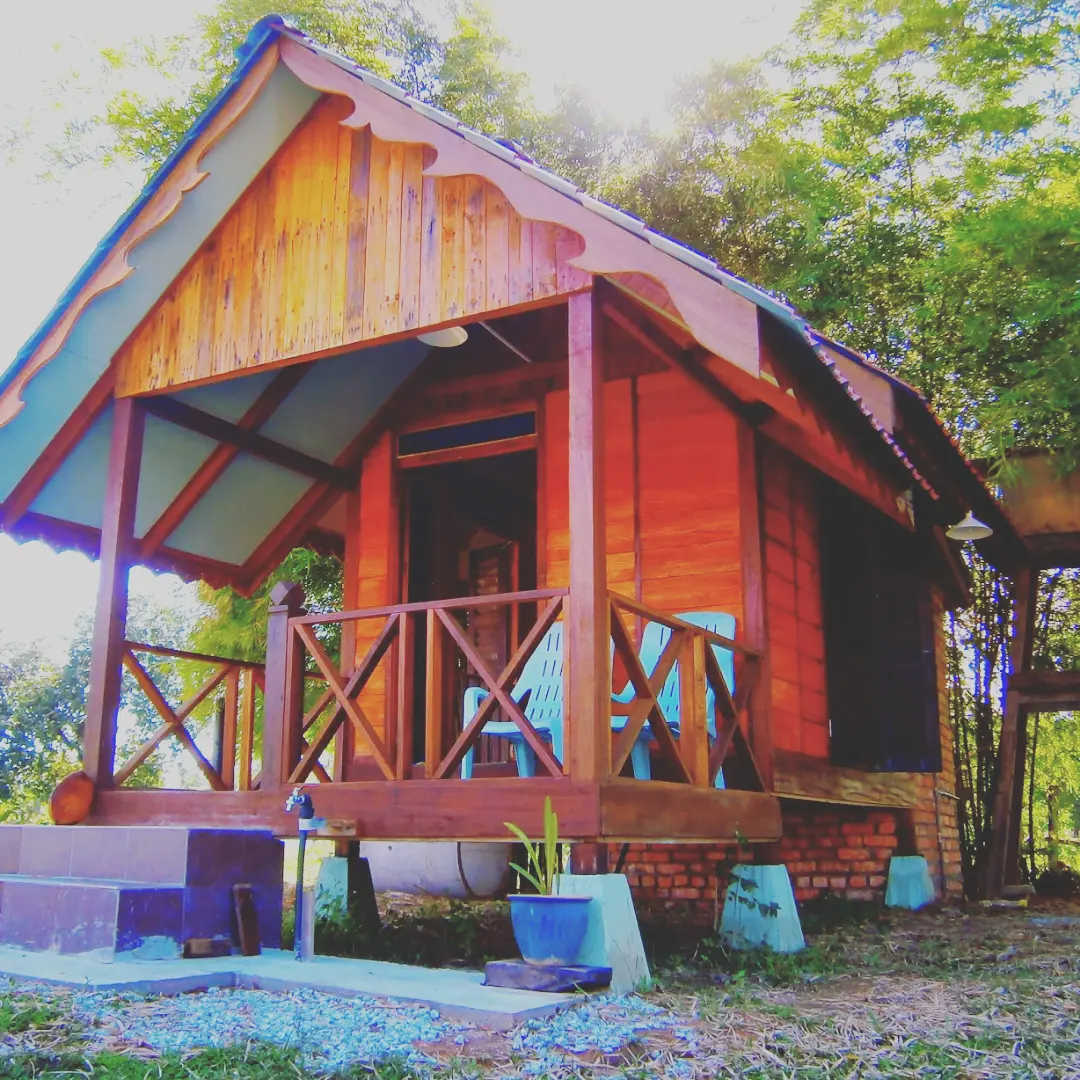 The Cottage Langkawi featuring a cozy traditional wooden chalet with a covered front porch, rustic timber architecture, and a tranquil setting surrounded by lush tropical trees and nature.