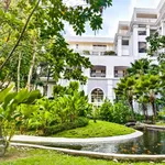 The Danna Langkawi featuring elegant colonial-inspired architecture surrounded by lush tropical gardens, manicured lawns, ornamental ponds with koi fish, and a serene luxury resort atmosphere.